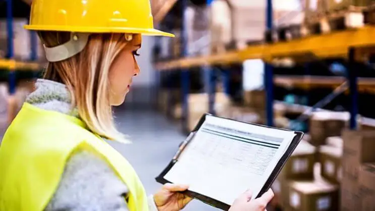 A woman in a warehouse reading shipping documents, representing freight cost calculation and logistics planning.